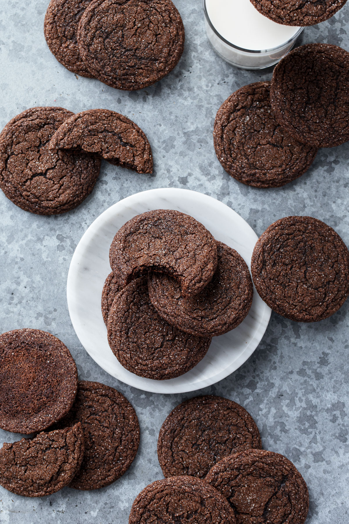 Overhead, plate of Chewy Chocolate Molasses Cookies on a gray background, one cookie with a bite out of it and more scattered around.