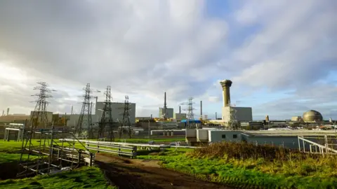 Getty Images An exterior shot of Sellafield, Cumbria, the nuclear site where 140 tonnes of plutonium is currently stored. The picture shows green grass and scrub in the foreground and a little further back, an industrial plant with pylons and silver-grey towers and a large round structure in the background, against a mottled sky of clouds with some blue sky and sunshine poking through.