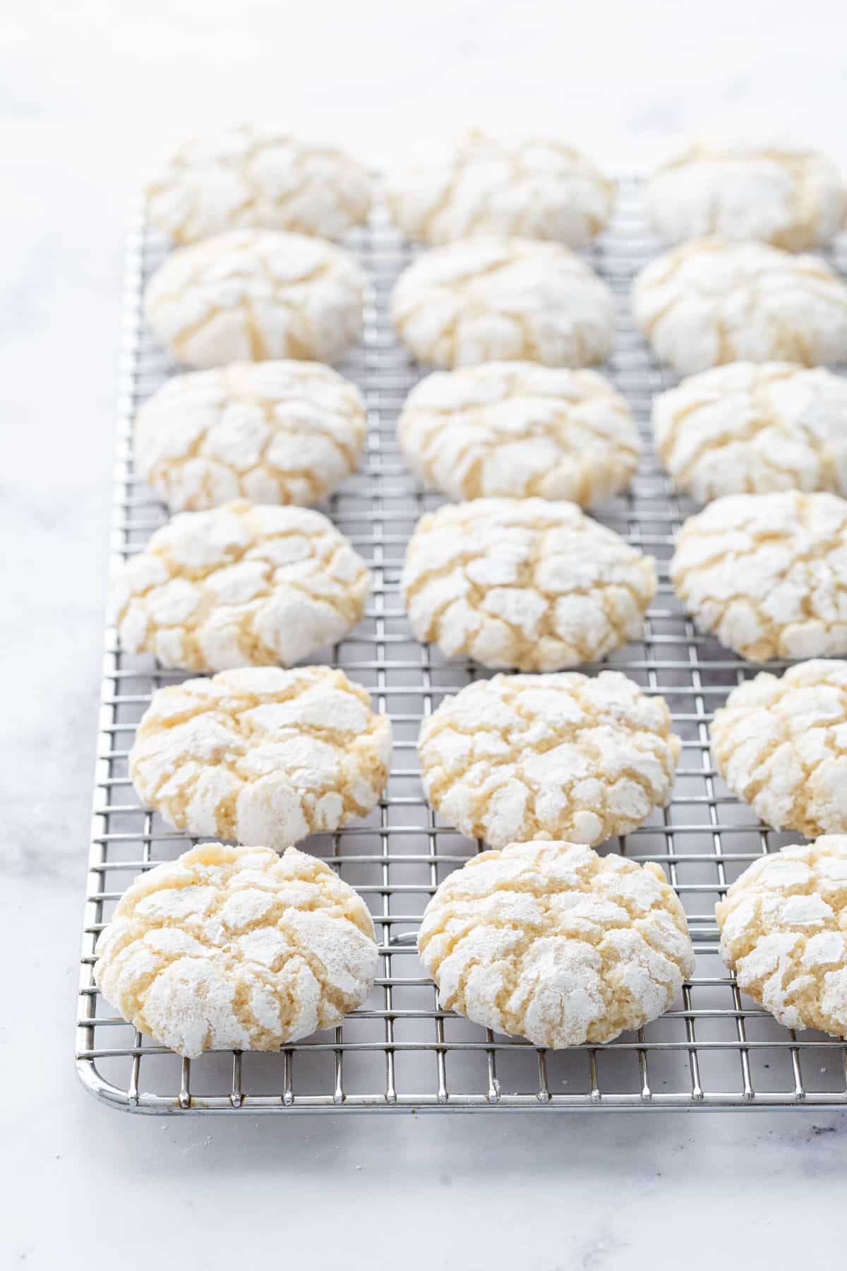 Even rows of Chewy Lemon Almond Crinkle Cookies on a wire baking rack sitting on a marble background.