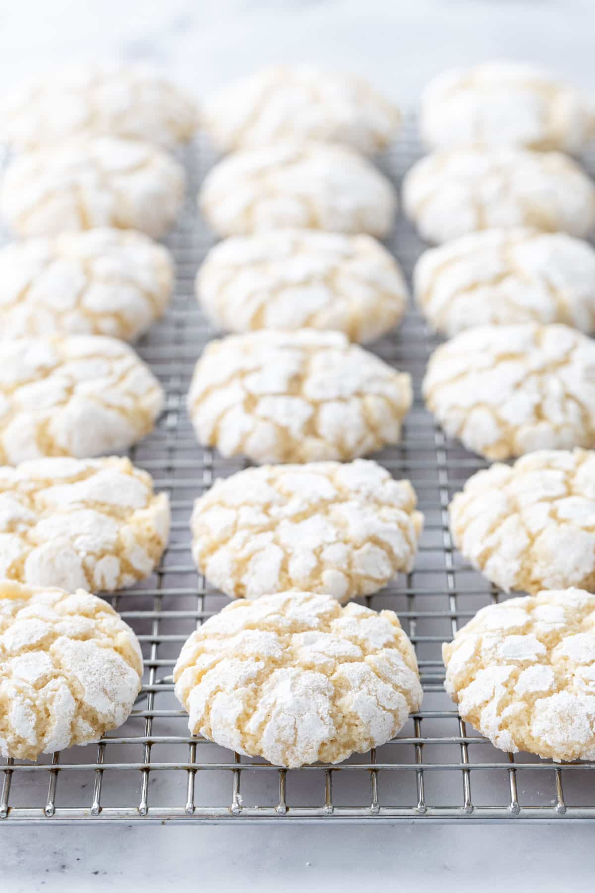 Even rows of Chewy Lemon Almond Crinkle Cookies on a wire baking rack sitting on a marble background.