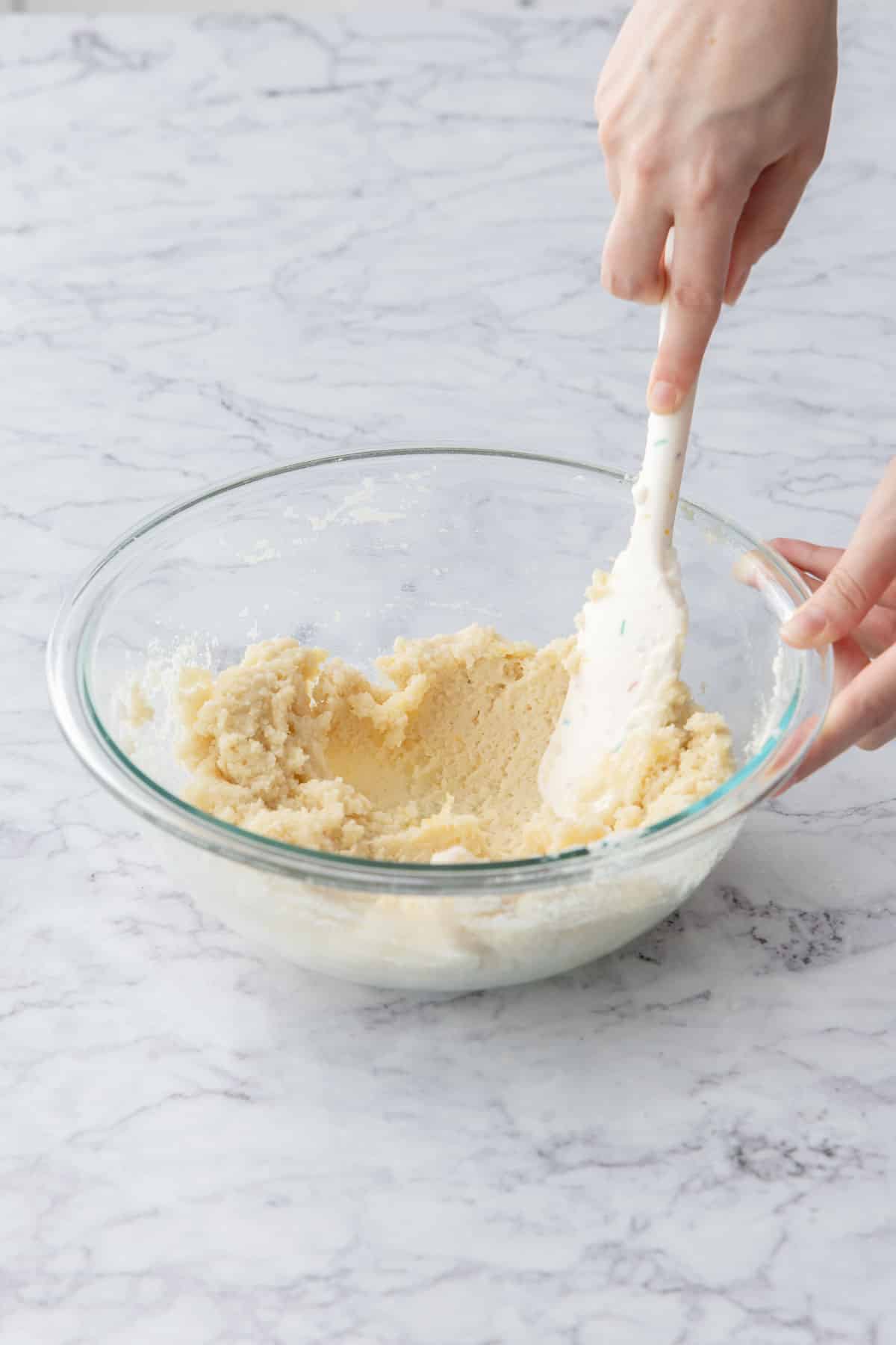 Spatula mixing Lemon Almond Crinkle Cookie dough in a glass mixing bowl.