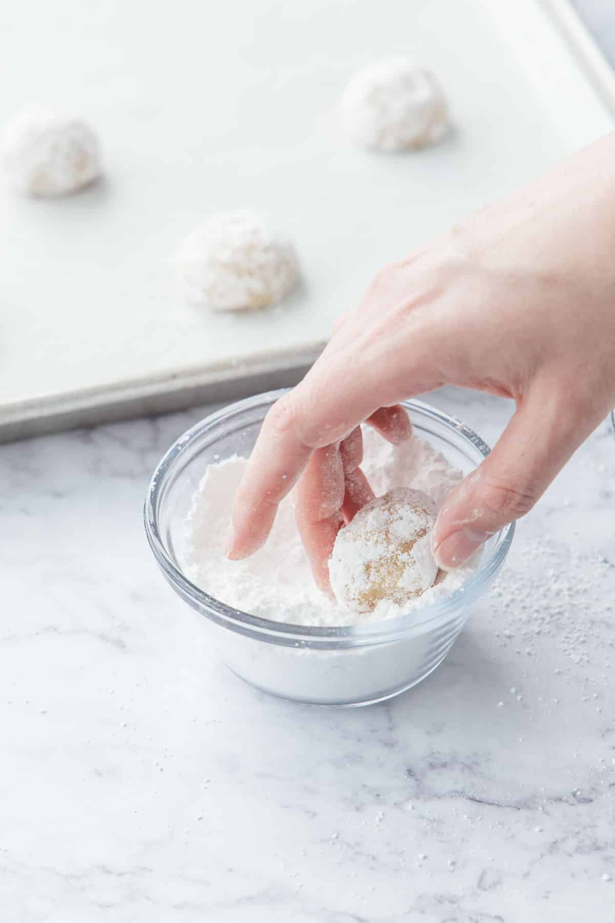 Rolling cookie dough balls in a small bowl of powdered sugar.