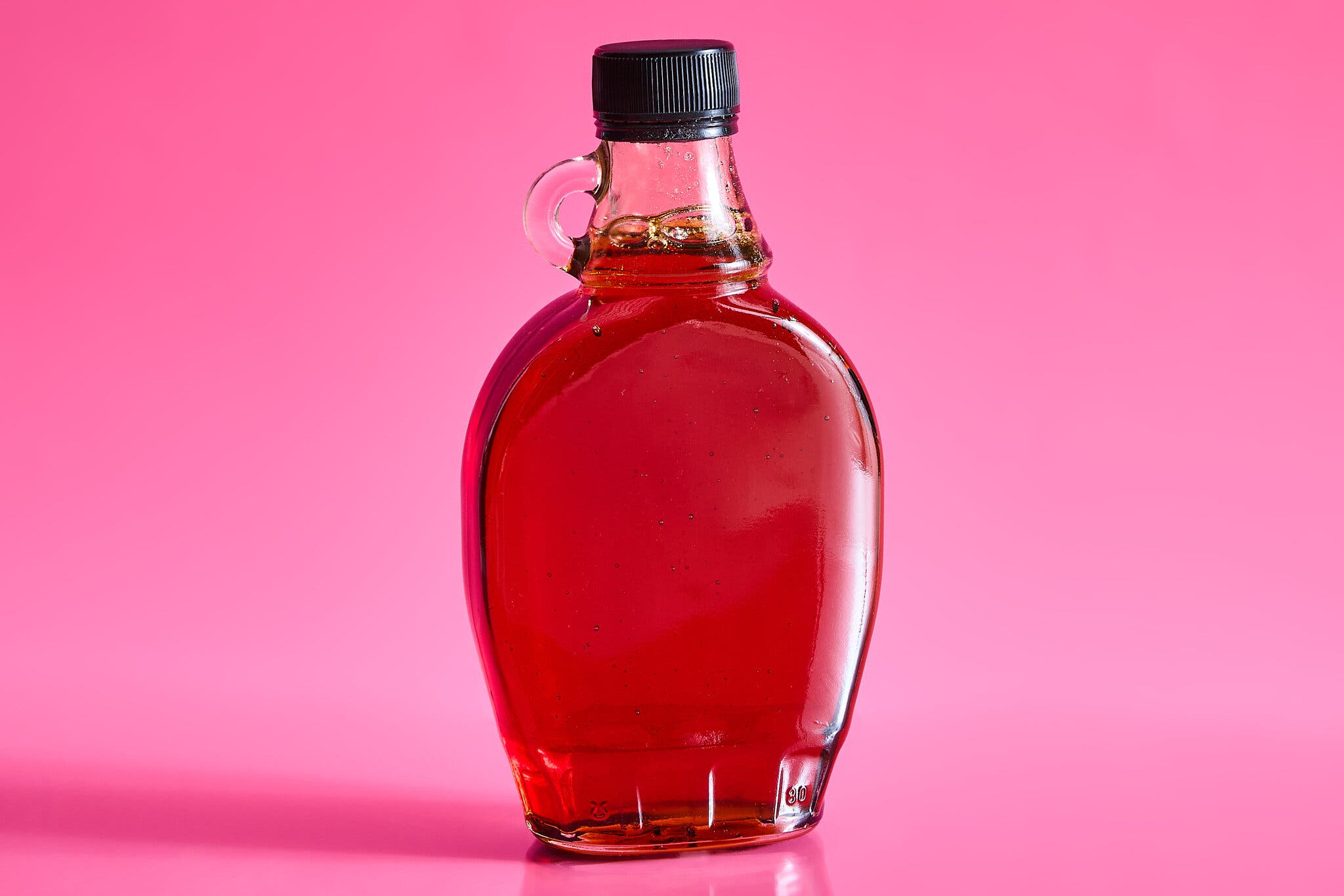 A bottle of maple syrup against a hot pink background.