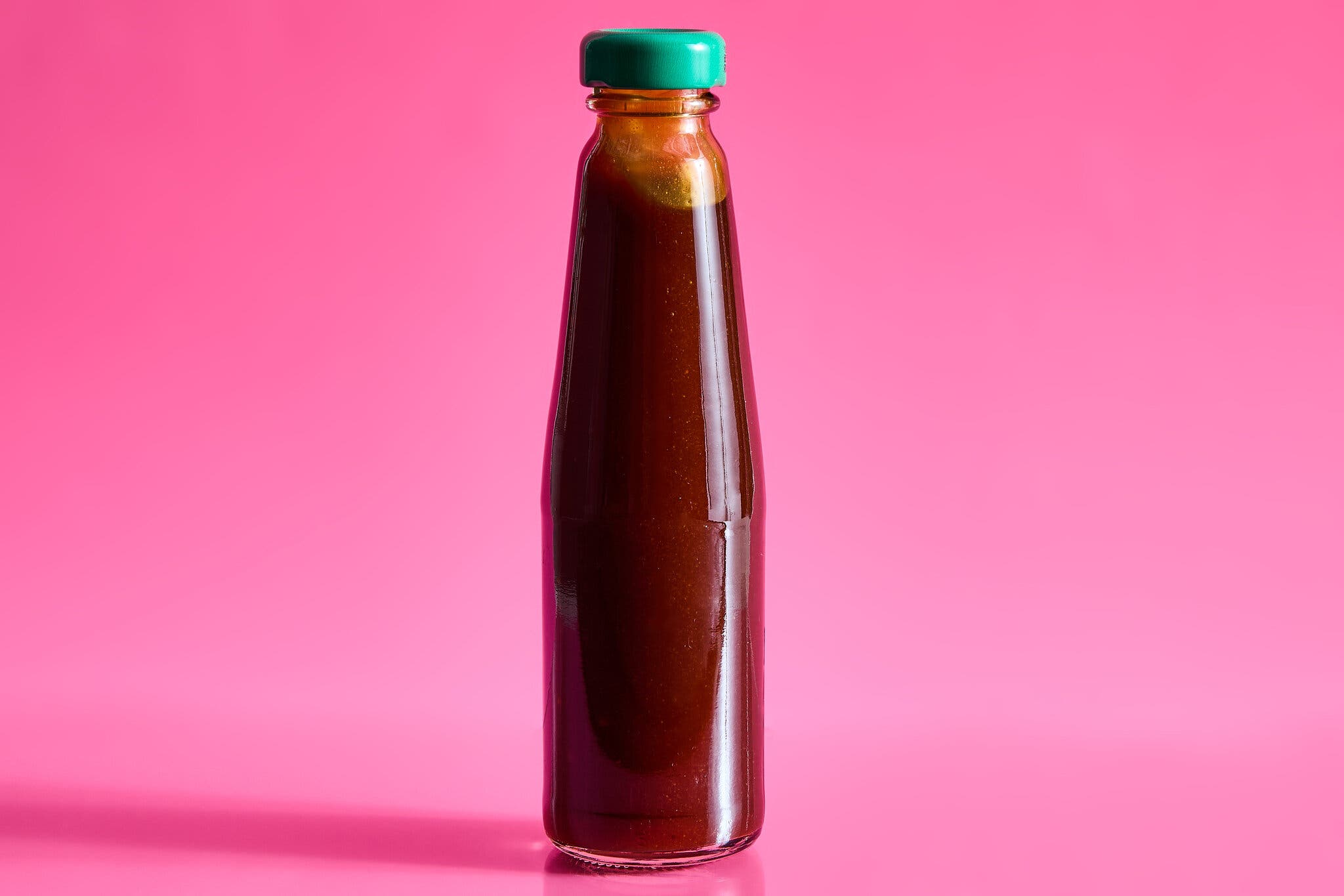 A tall bottle of oyster sauce against a hot pink background.