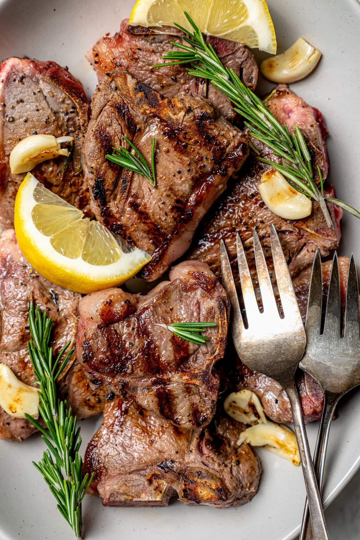 With fragrant rosemary and garlic, this easy grilled lamb chops recipe is flavorful, succulent, and one I love to cook all year long! Overhead view of grilled lamb chops on platter with fresh rosemary, lemon wedges, and garlic cloves