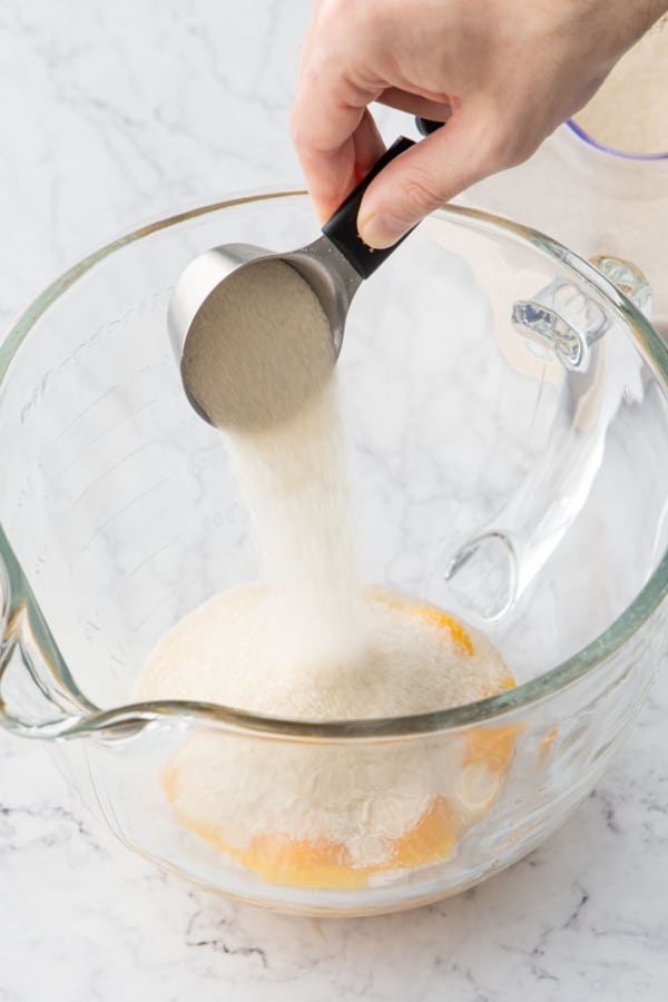Pouring organic sugar into a mixing bowl with egg yolks.
