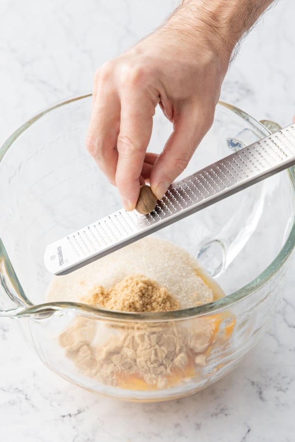 Grating fresh nutmeg into a mixing bowl with egg yolks and sugar.