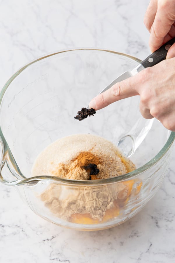 Adding the seeds of a fresh vanilla bean to the mixing bowl.