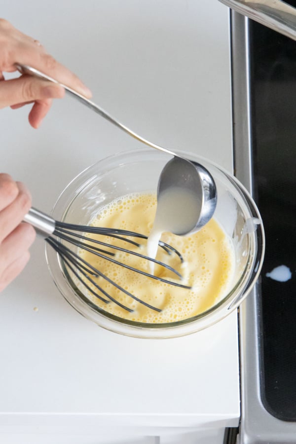 Tempering egg yolks with warm milk mixture.