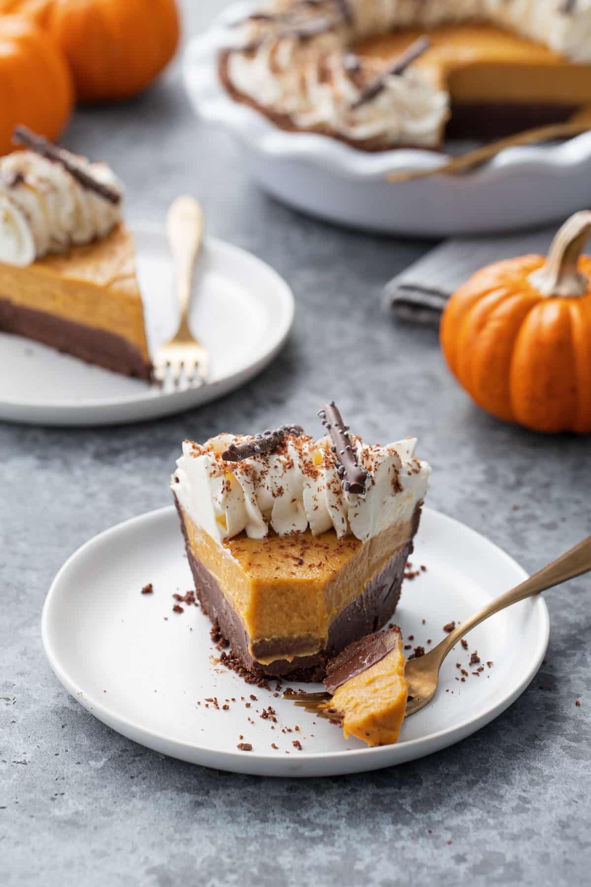 Slice ofBlack Bottom Pumpkin Cream Pie on a plate with a bite sitting on a gold fork, with mini pumpkins in the background.