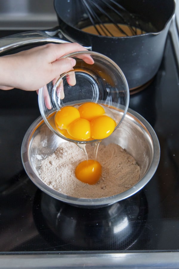 Adding egg yolks to a bowl with sugar, flour, cornstarch, salt, and pumpkin spice.