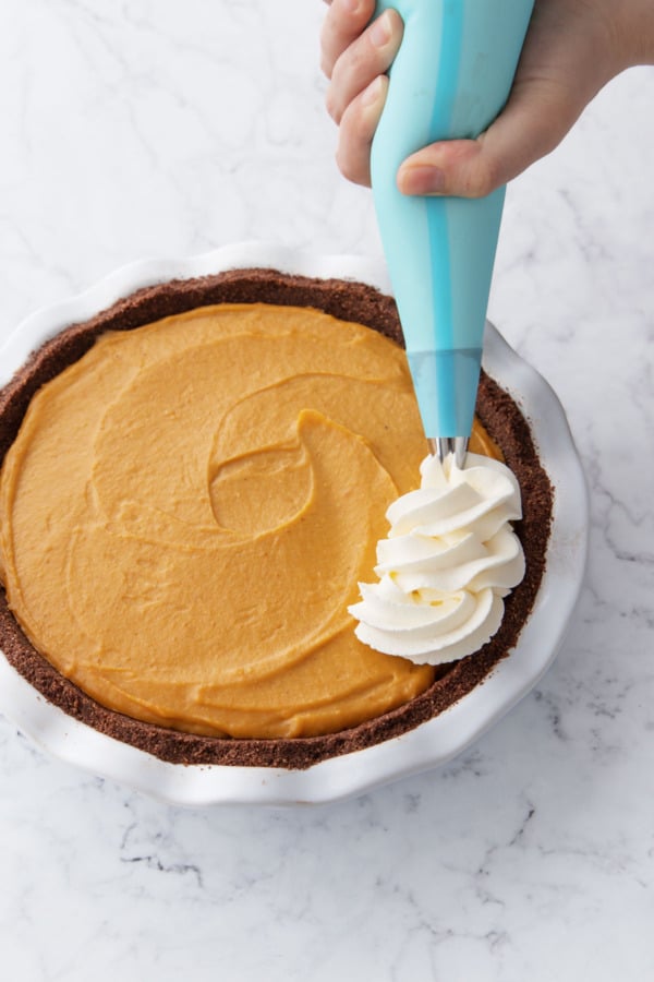Piping a border of whipped cream around the edge of the cream pie.